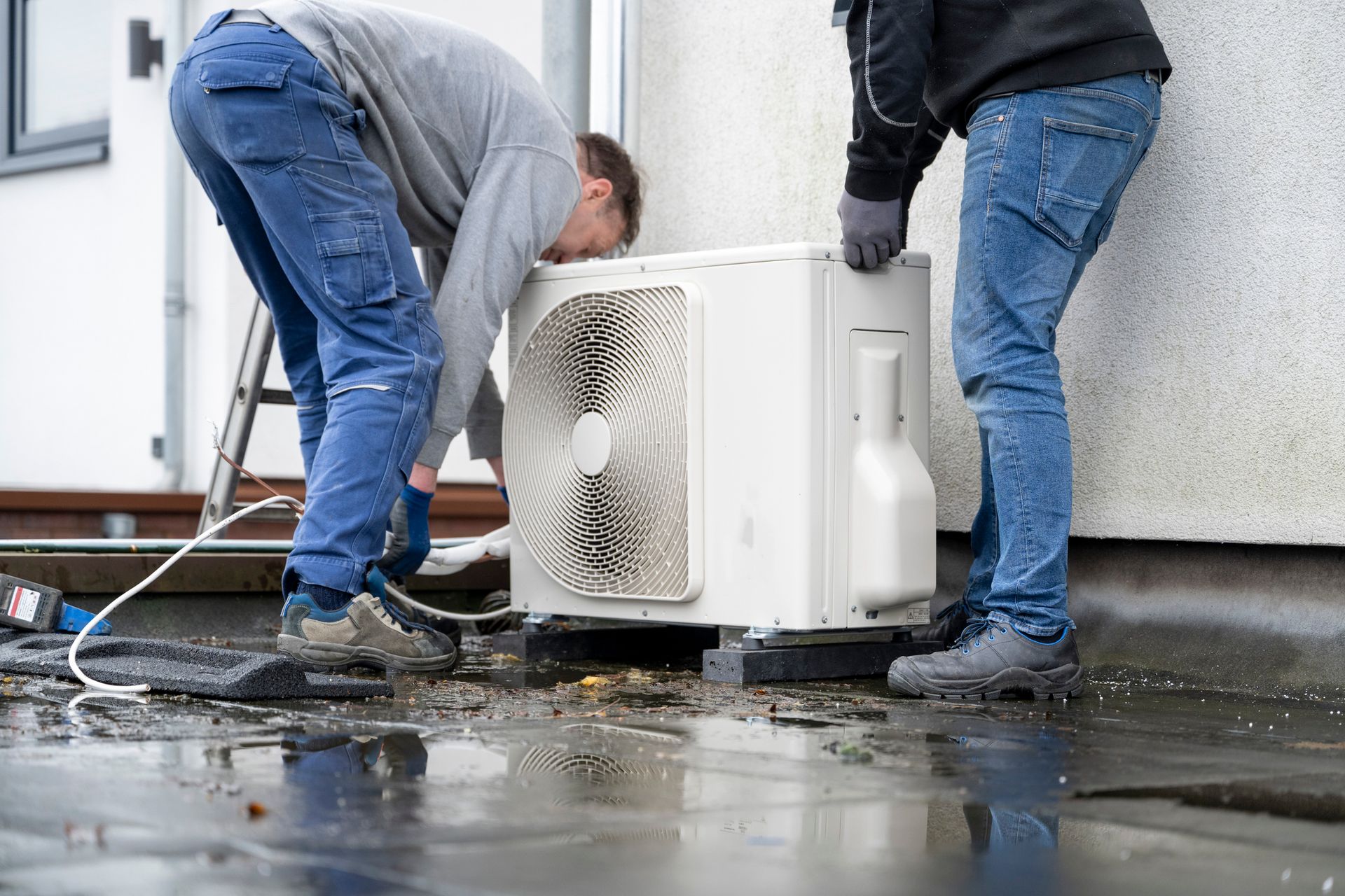 Two men are working on an air conditioner outside of a building.
