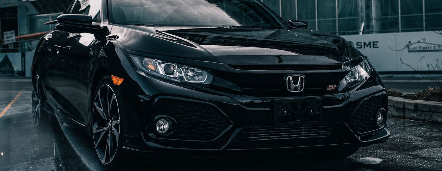 Black Honda Civic in the rain, front view with headlights on, parked on a wet street