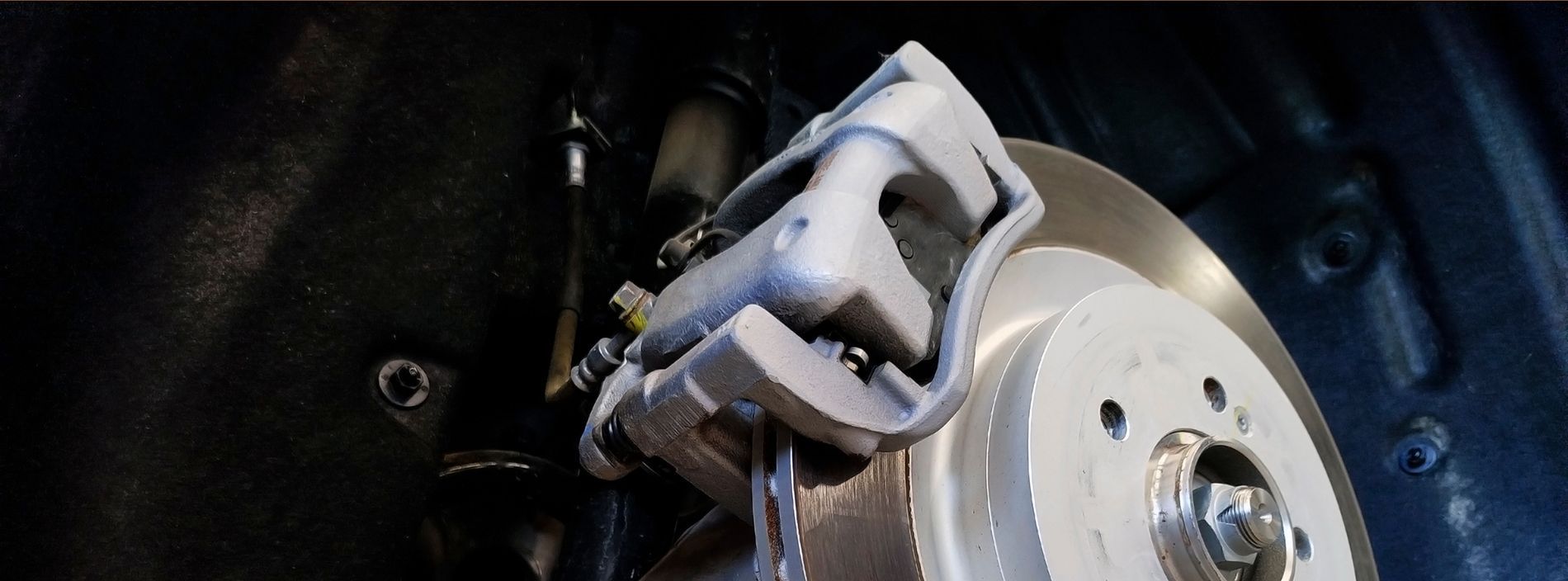 Car brake assembly: caliper, rotor, and suspension components, likely for maintenance or repair.