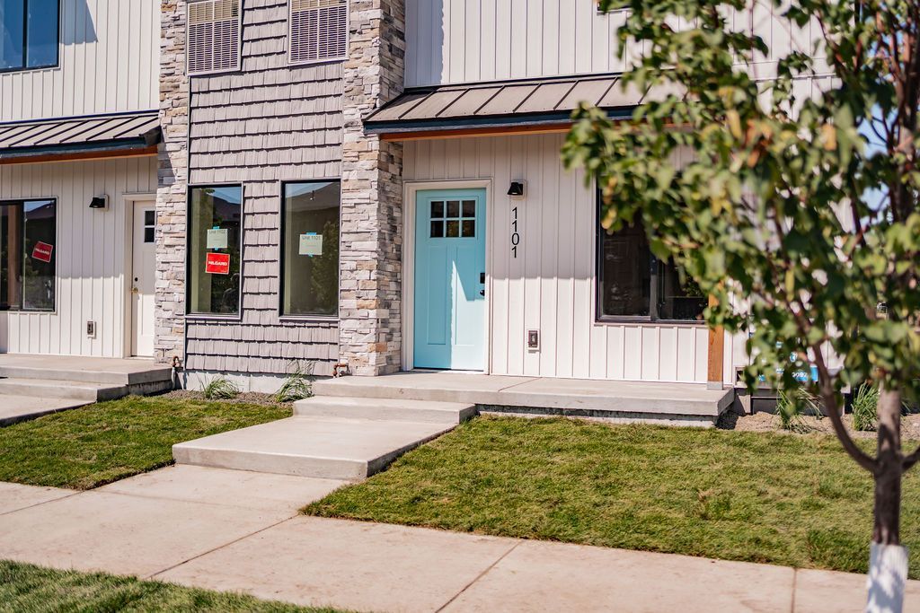Row of townhouses with blue door, stone and white siding, and small front lawns.