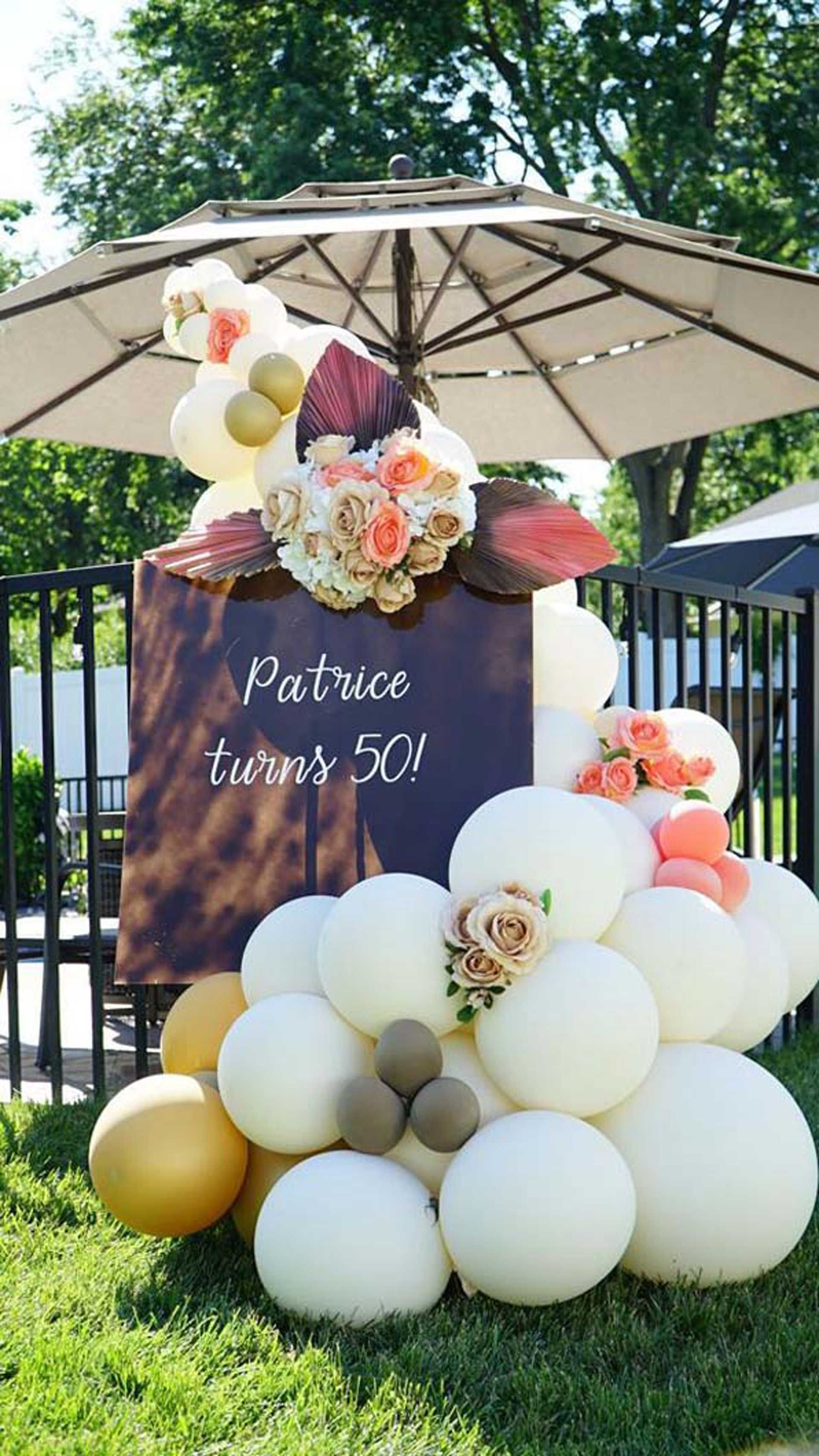 A sign that says Patrice turns 50 is surrounded by balloons and flowers