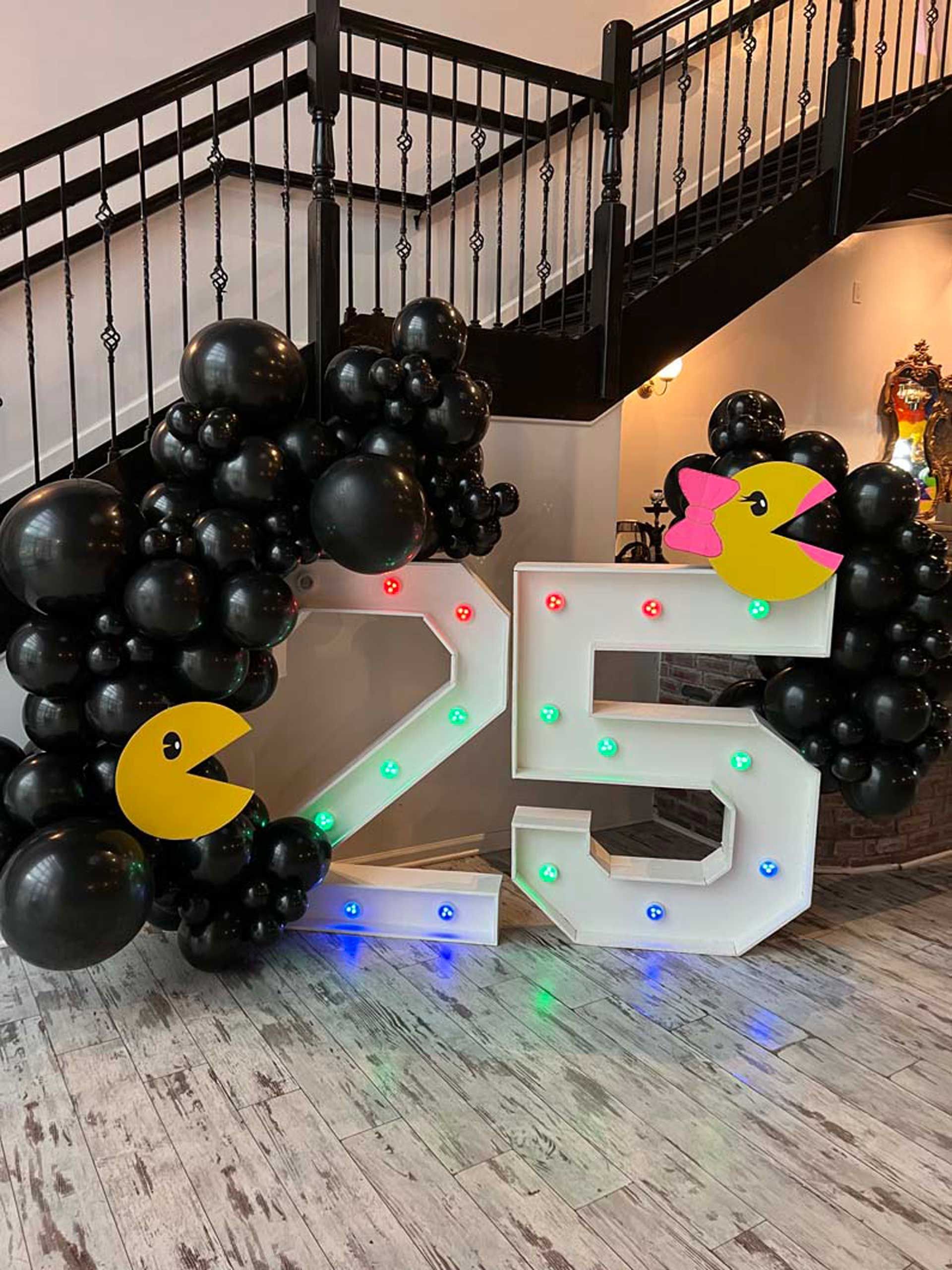 A large number 25 is surrounded by black balloons and Pac man
