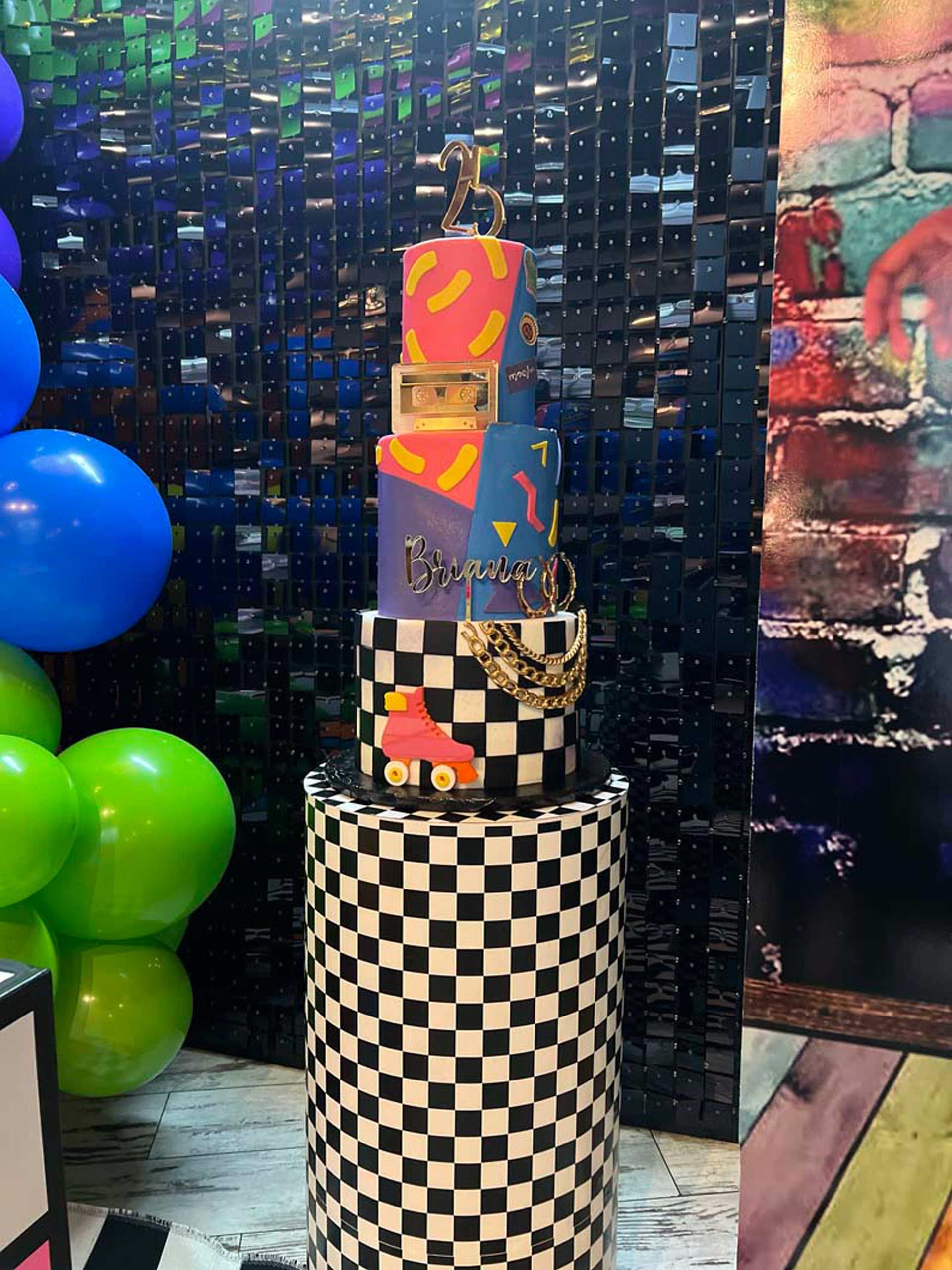 A colorful cake is sitting on top of a black and white checkered pedestal