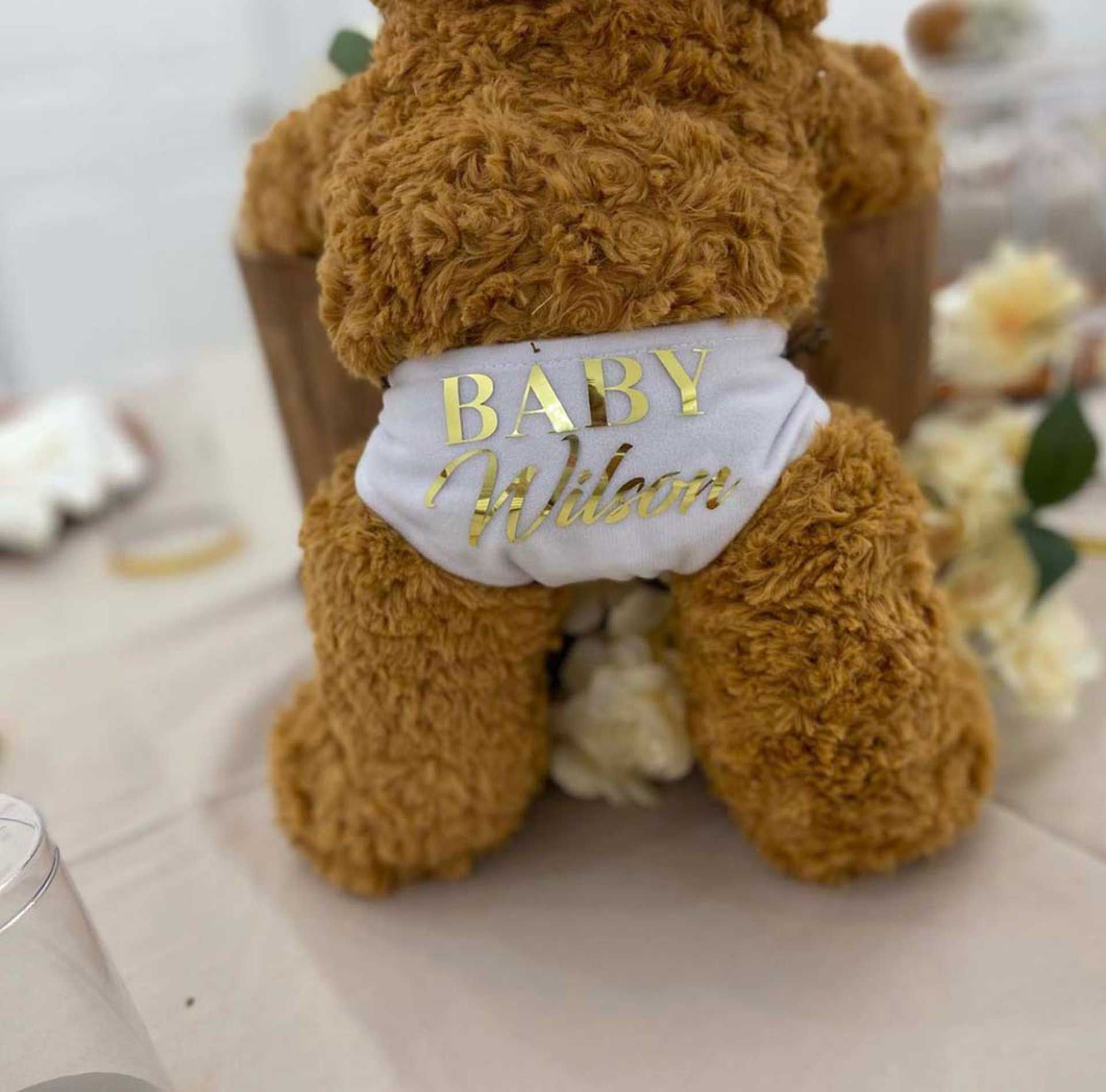 A teddy bear wearing a baby welcomes shirt is sitting on a table