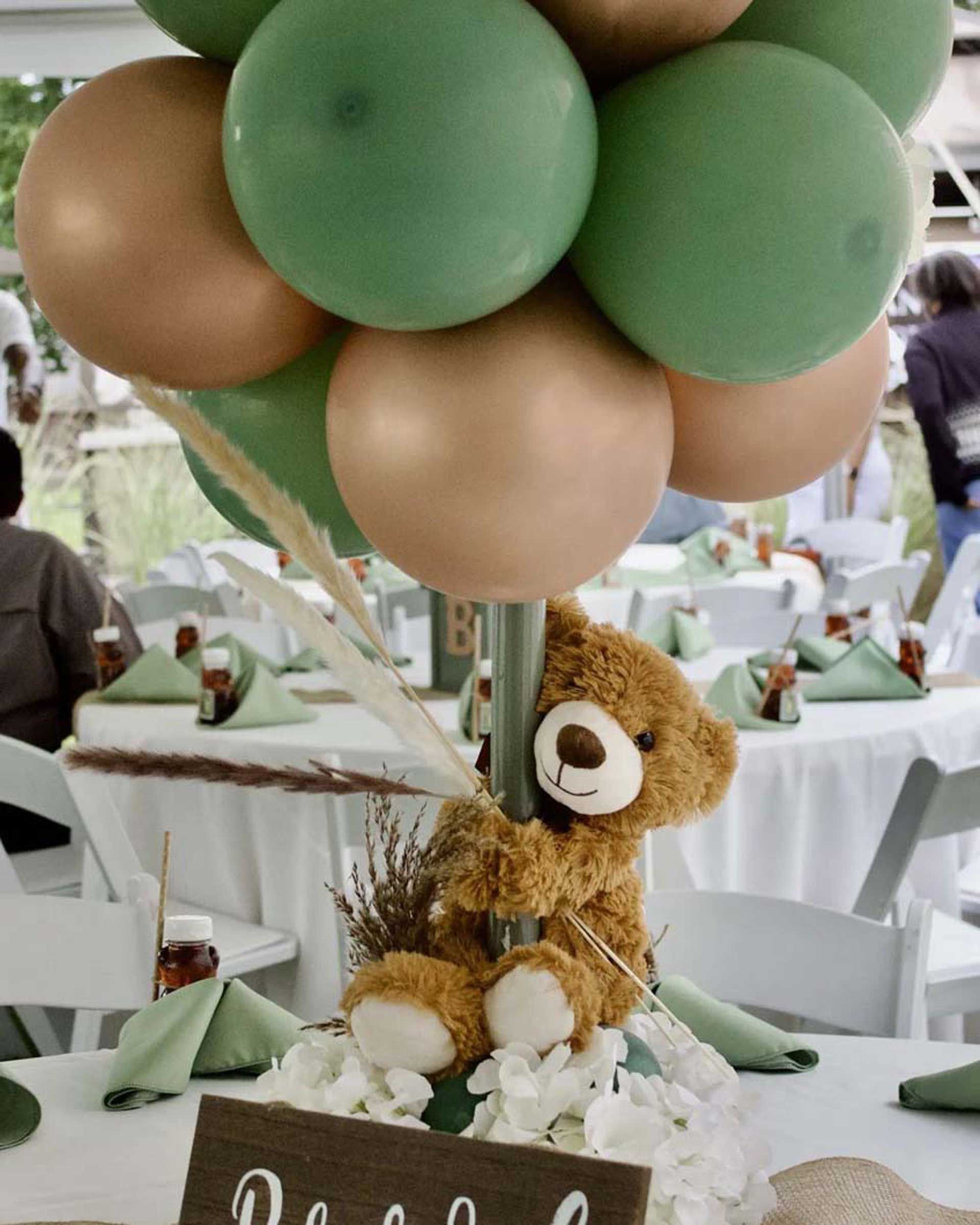 A teddy bear is sitting under a bunch of green and gold balloons