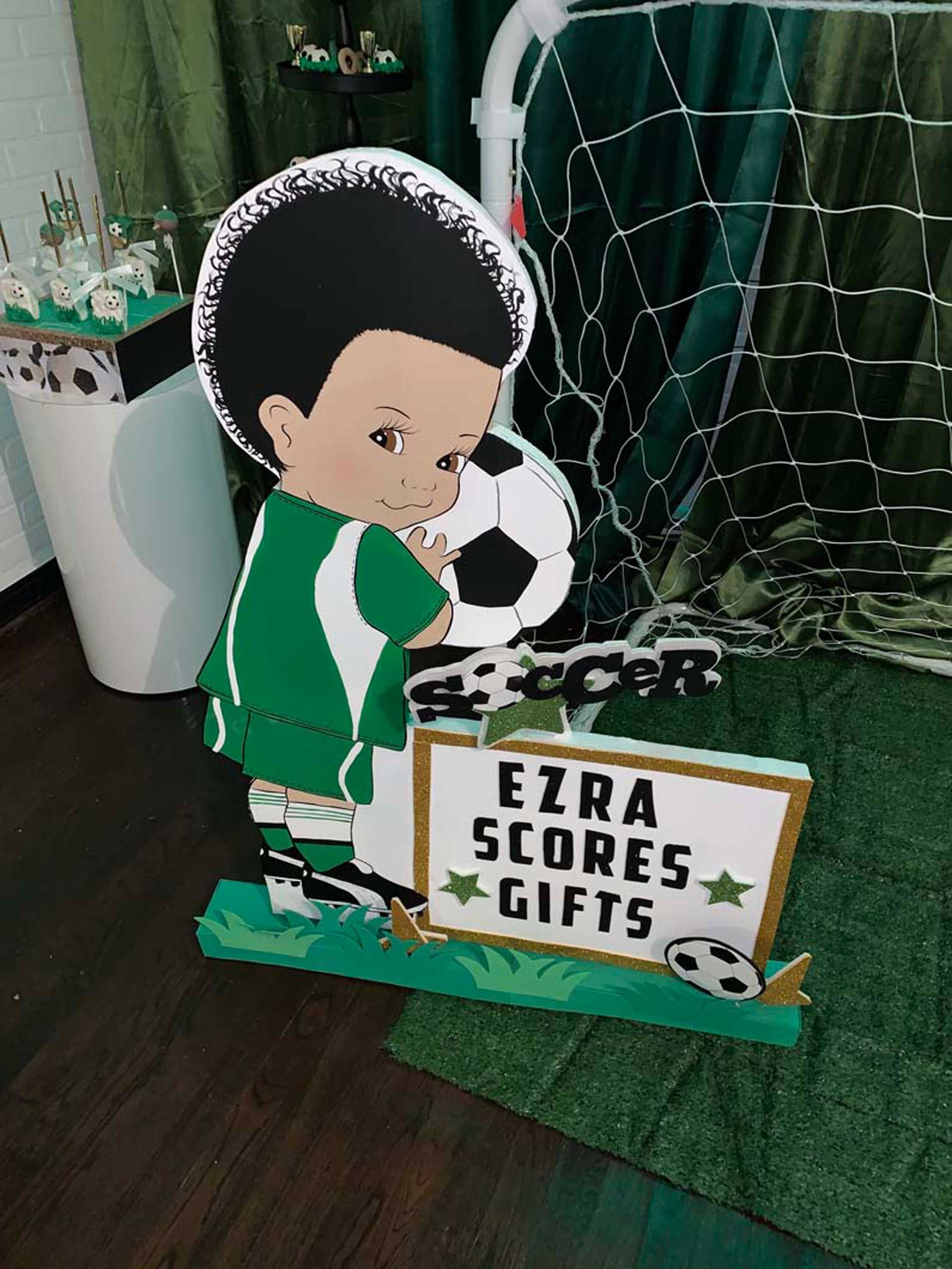 A boy holding a soccer ball next to a sign that says Ezra scores gifts