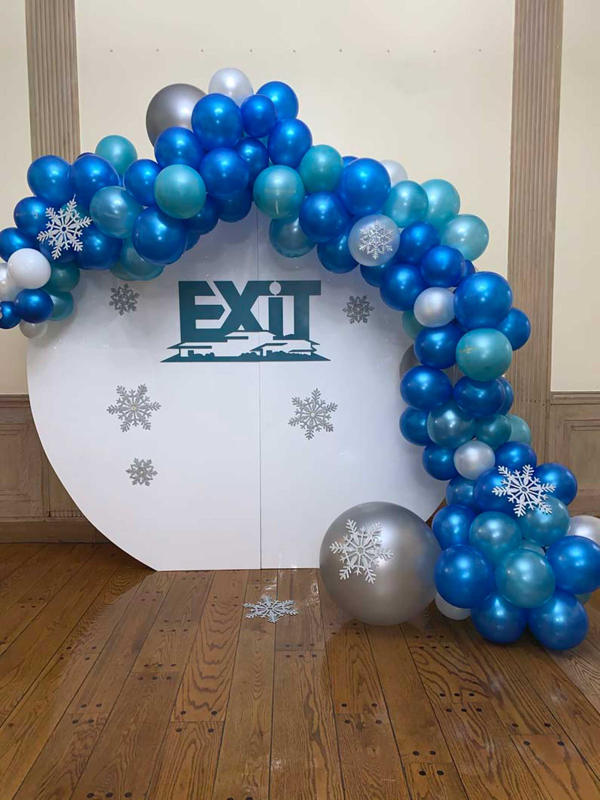 A white sign with the word exit on it is surrounded by blue and silver balloons