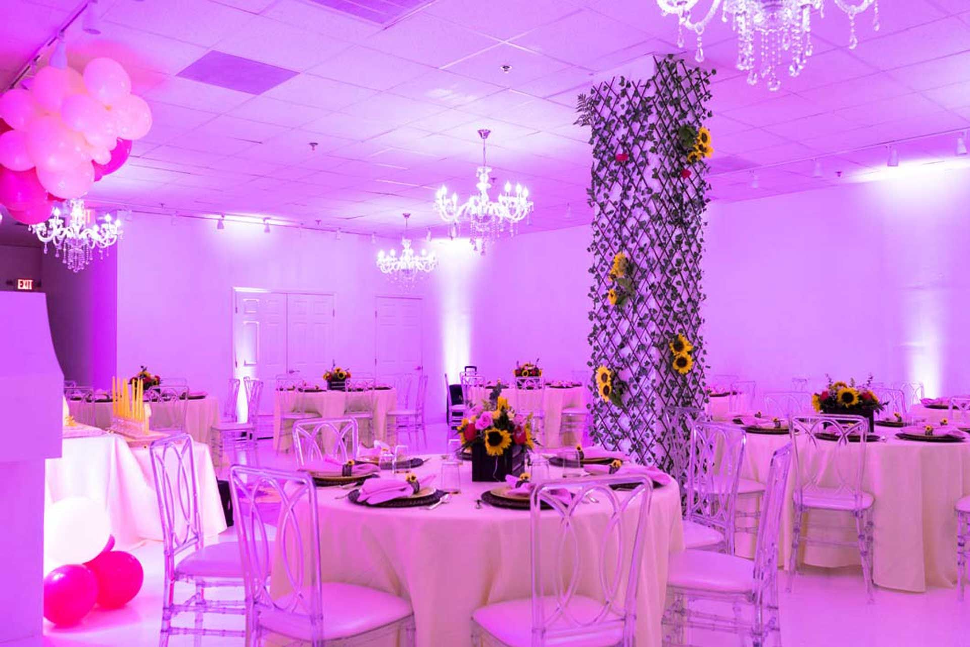 A large room with tables and chairs set up for a party with purple lights