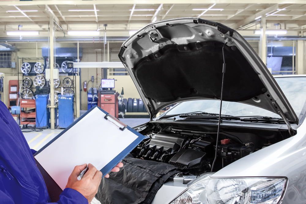 A Mechanic is Looking at a Clipboard in Front of a Car With the Hood Up — Edgy Car Mechanics in Edgeworth, NSW