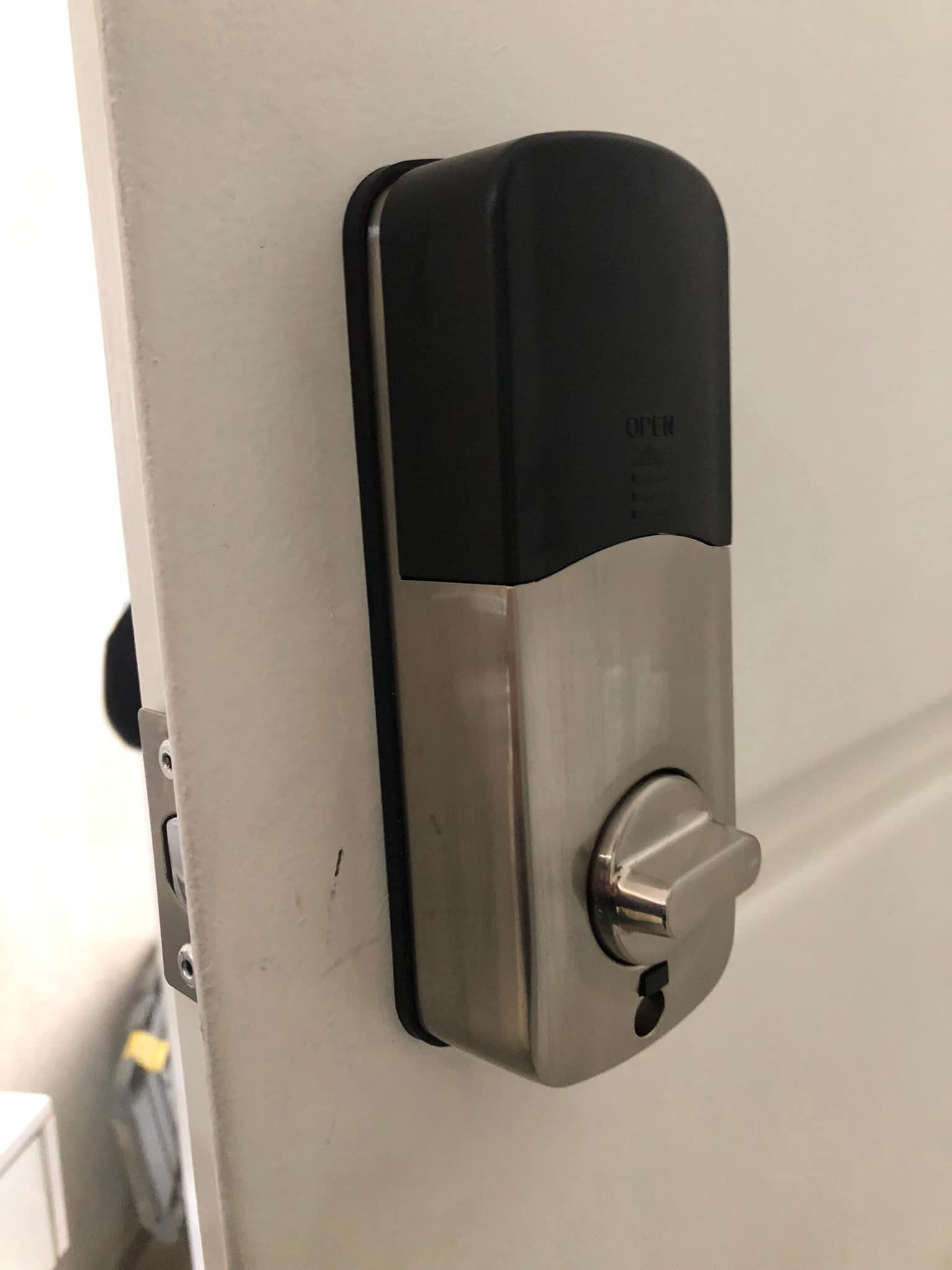 Cerradura de puerta inteligente en puerta blanca, carcasa plateada y negra, manija de la puerta visible.