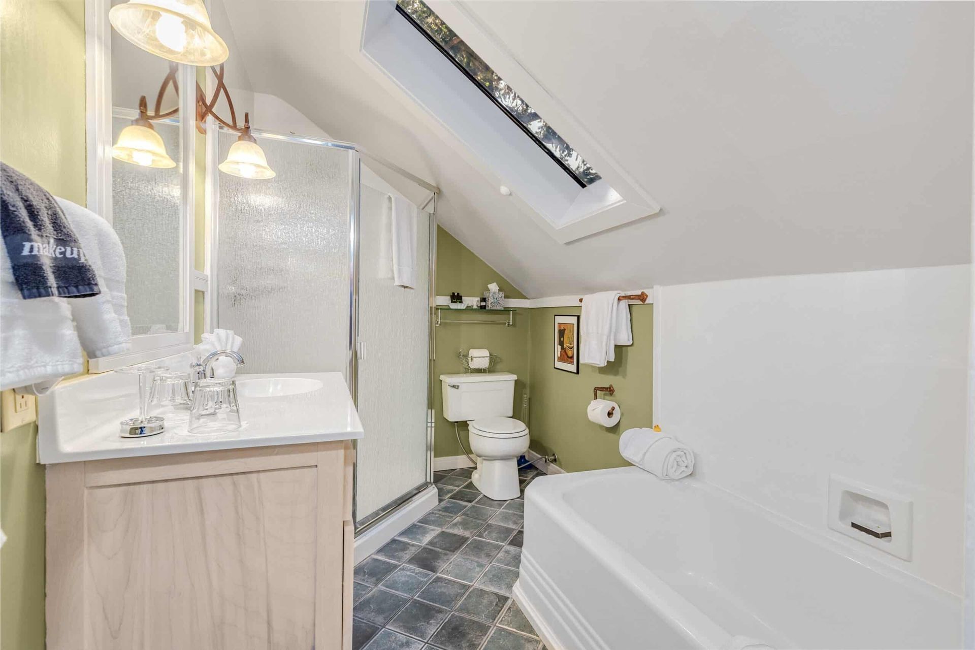 A bathroom with a sink , toilet , bathtub and skylight.