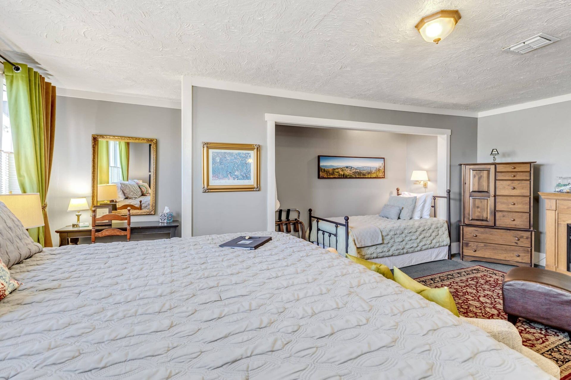 A bedroom with two beds , a dresser and a fireplace.