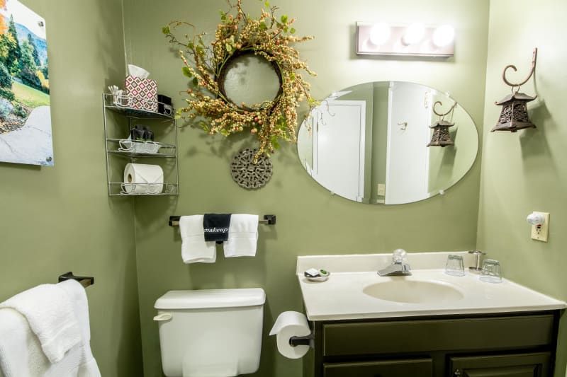 A bathroom with a toilet , sink , mirror and wreath on the wall.