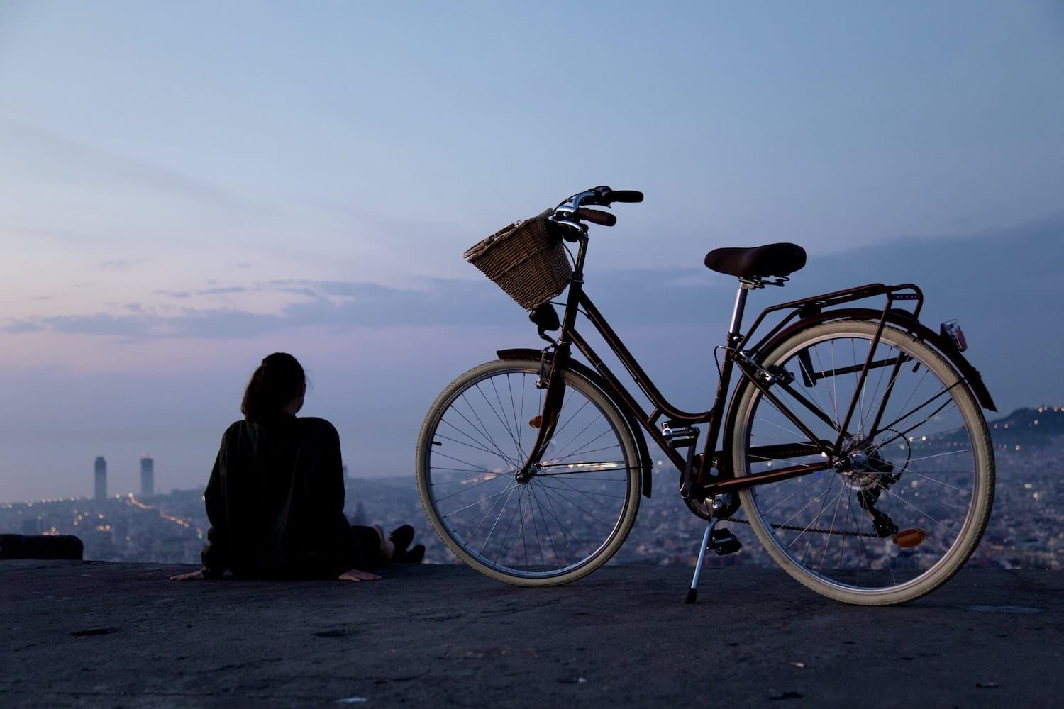 A woman is sitting on a hill next to a bicycle.