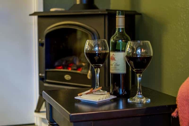 A bottle of wine and two glasses of wine are on a table in front of a fireplace.