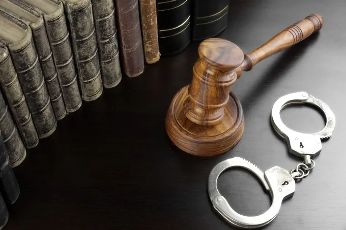 Wooden gavel, silver handcuffs, and law books on a dark surface.