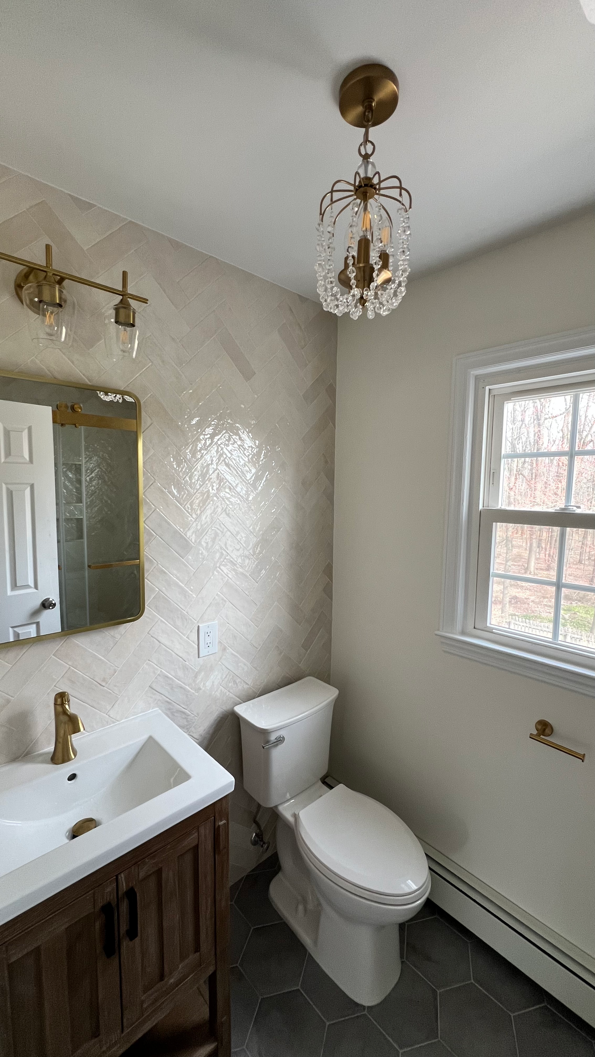 A bathroom with a toilet , sink , mirror and window.