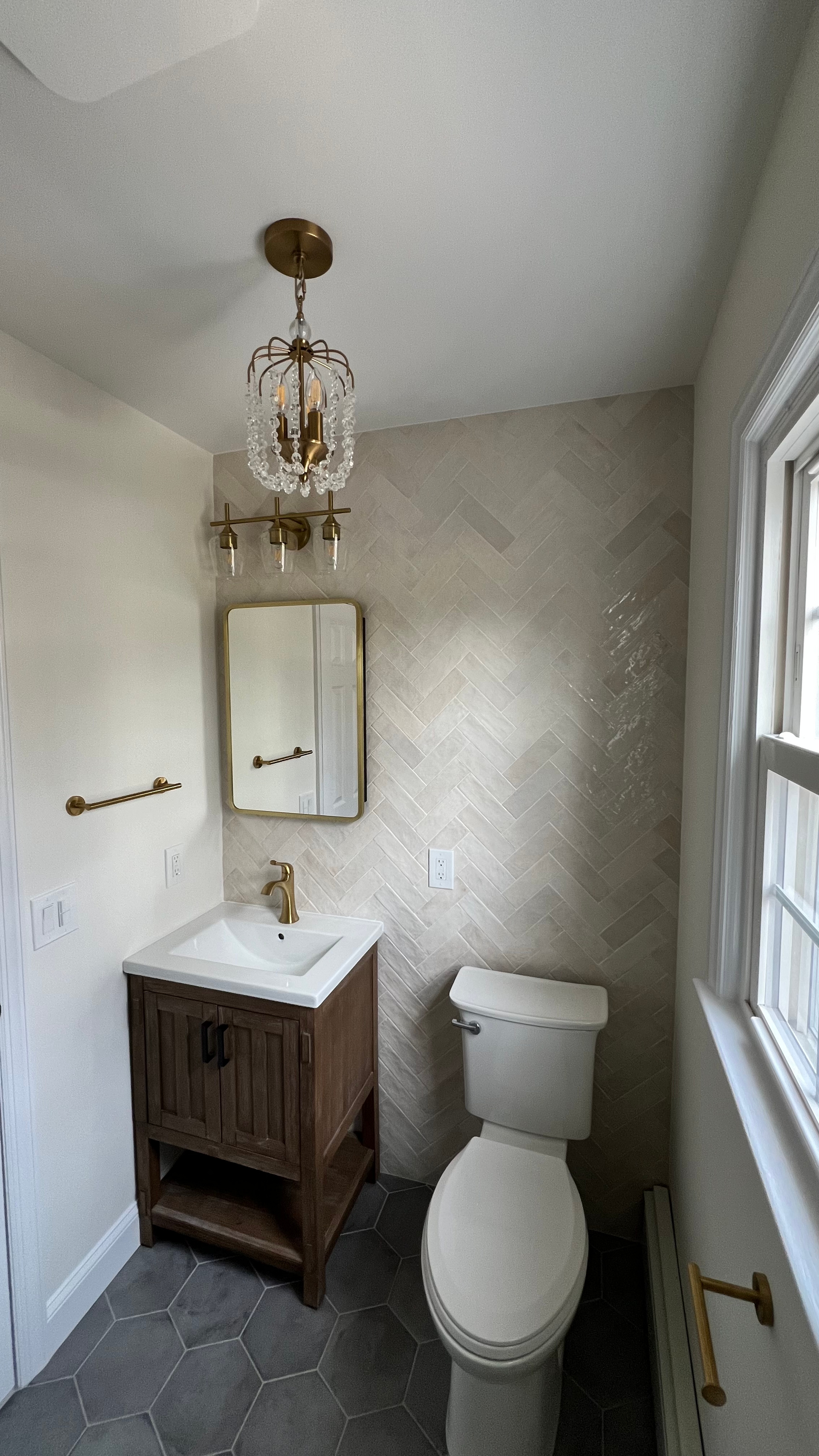 A bathroom with a toilet , sink , mirror and window.