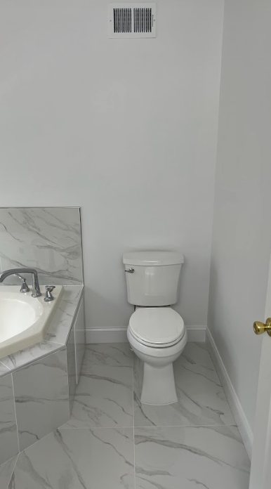 A bathroom with a toilet , sink and marble floor.