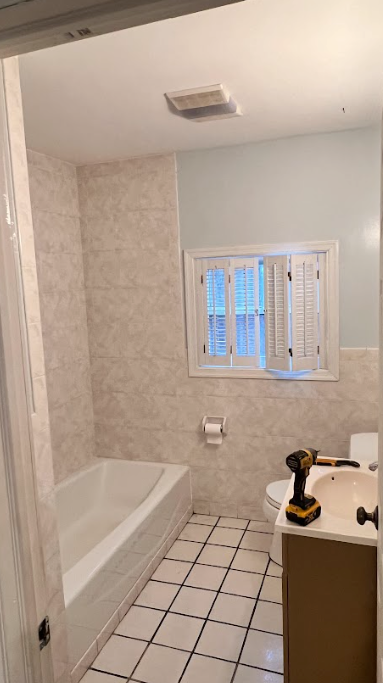 A bathroom with a tub , sink , toilet and window.