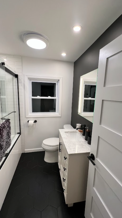 A bathroom with a toilet , sink , mirror and window.