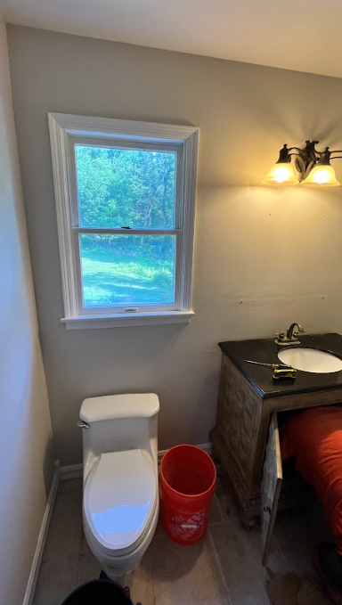 A bathroom with a toilet , sink , and window.