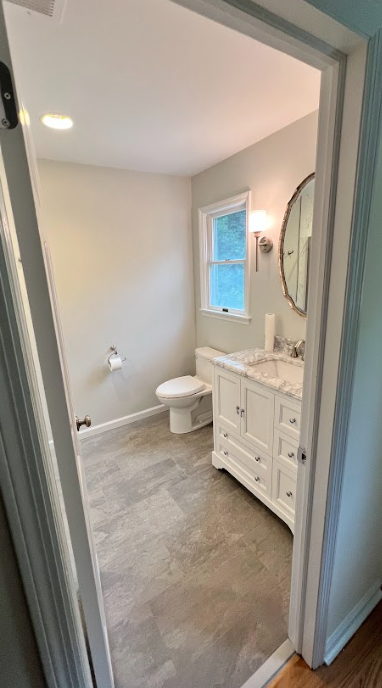 A bathroom with a toilet , sink , mirror and window.