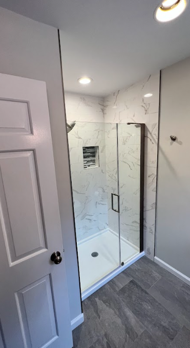 A bathroom with a walk in shower and a glass door.