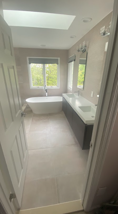 A bathroom with two sinks , a tub and a skylight.