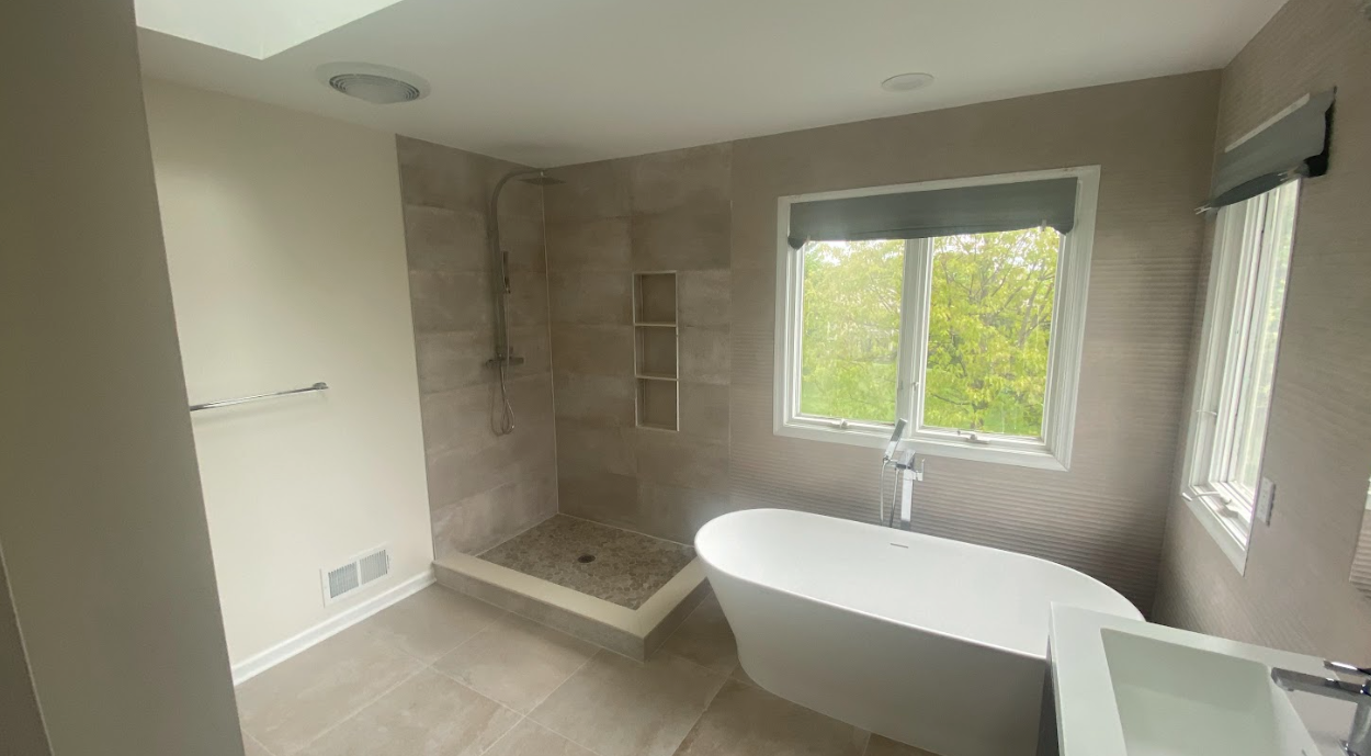 A bathroom with a tub , sink , shower and window.