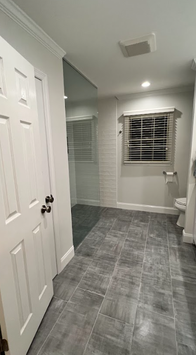 A bathroom with a toilet , shower , and window.