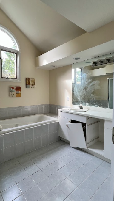 A bathroom with a tub , sink , mirror and window.