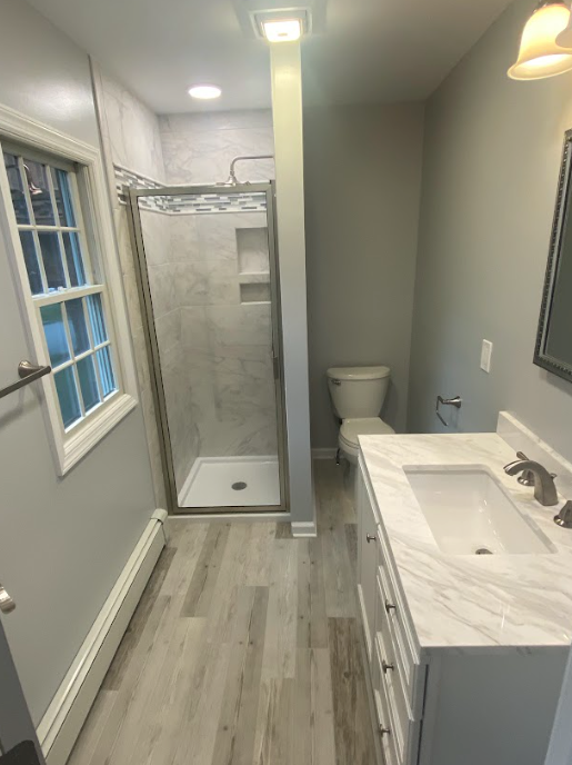 A bathroom with a sink , toilet , shower and window.