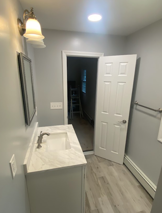 A bathroom with a sink , mirror and door.