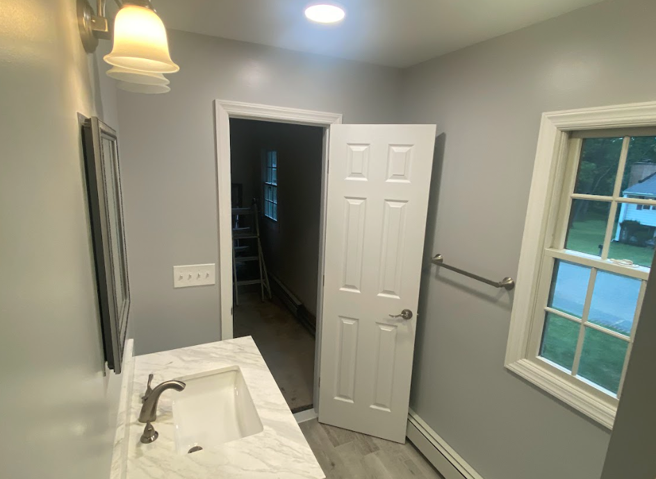 A bathroom with a sink , mirror and window.