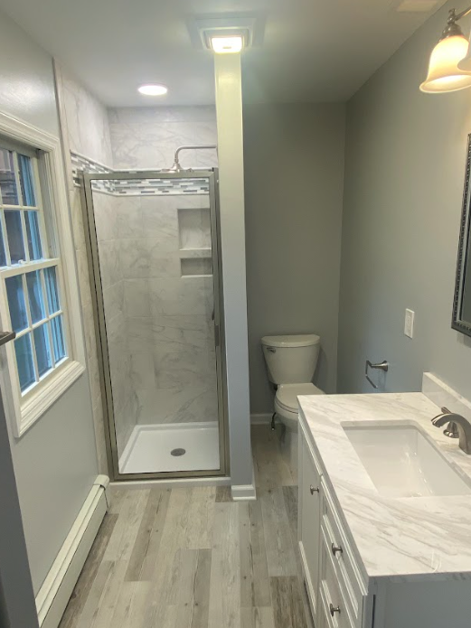 A bathroom with a sink , toilet , shower and window.