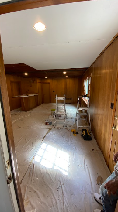 A room with wood paneling and a ladder in it is being painted.