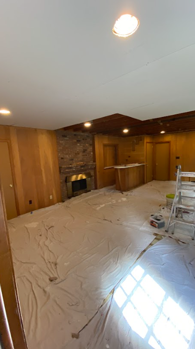A living room with a fireplace and a ladder in it is being painted.