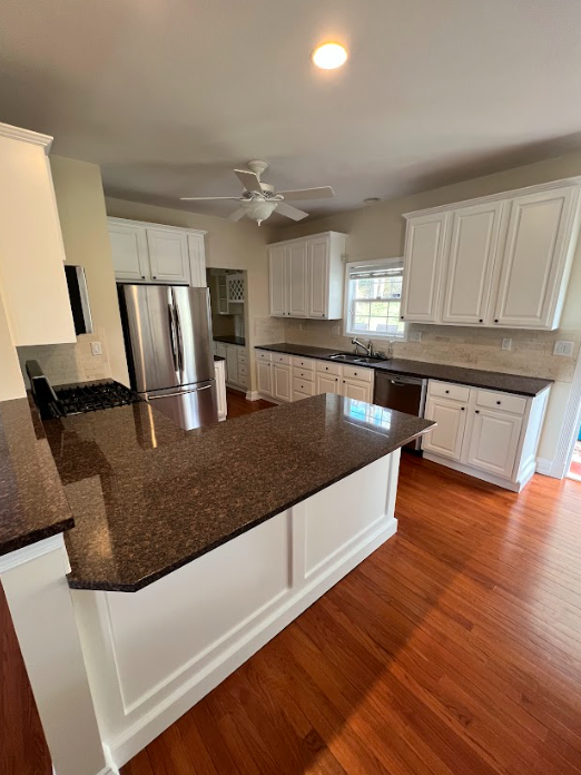 A kitchen with white cabinets , granite counter tops , stainless steel appliances and hardwood floors.