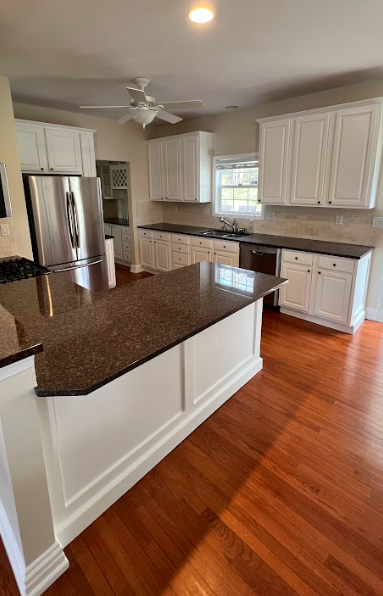 A kitchen with white cabinets , granite counter tops , stainless steel appliances and hardwood floors.