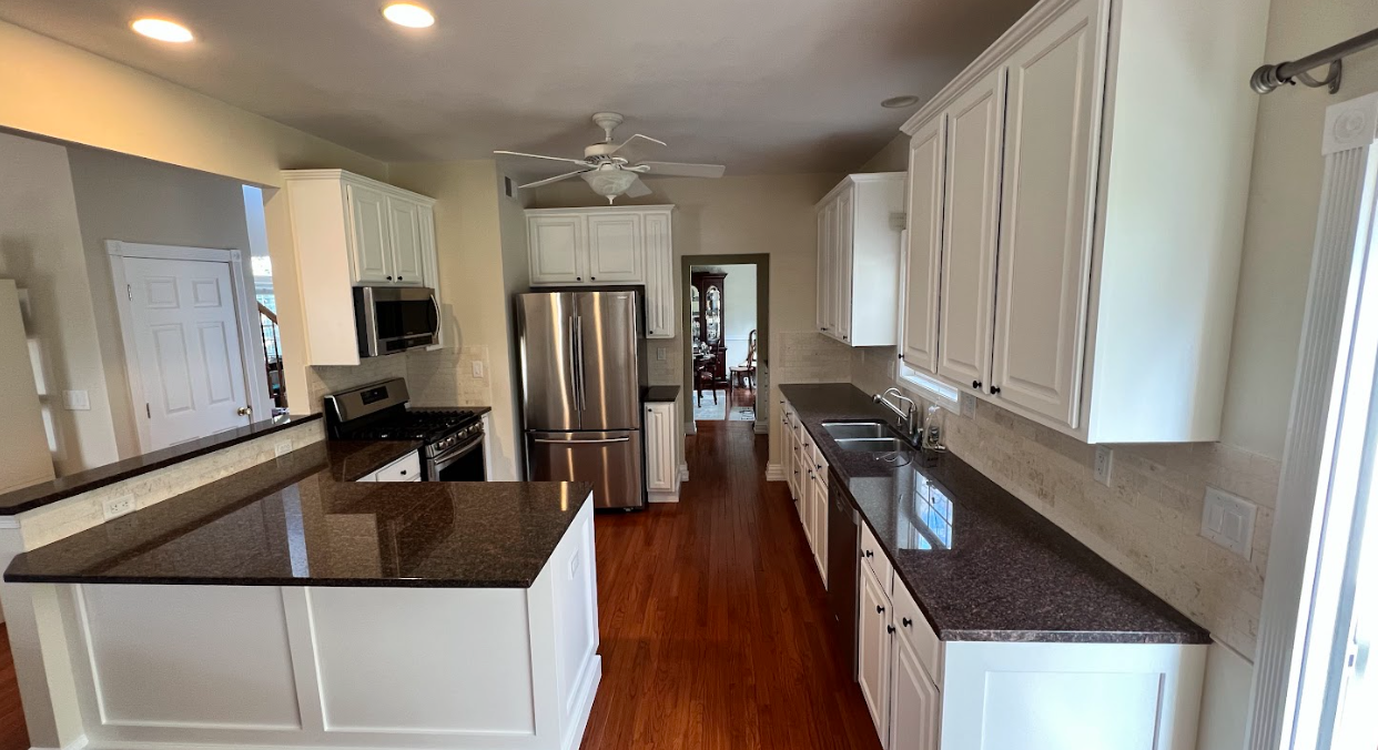 A kitchen with white cabinets , granite counter tops , stainless steel appliances and hardwood floors.