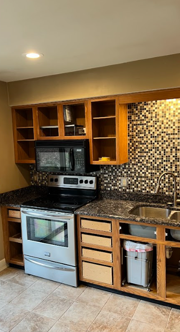 A kitchen with a stove , microwave , sink and cabinets.