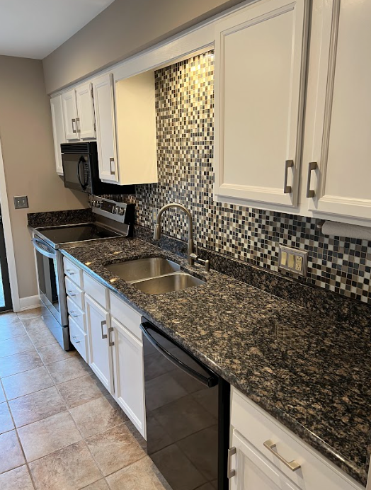 A kitchen with granite counter tops , stainless steel appliances , and white cabinets.