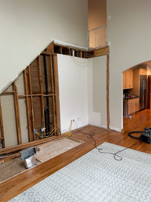 A living room with a staircase in the corner and a rug on the floor.