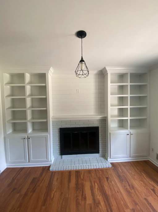 An empty living room with a fireplace and shelves