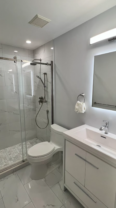 A bathroom with a toilet , sink , shower and mirror.