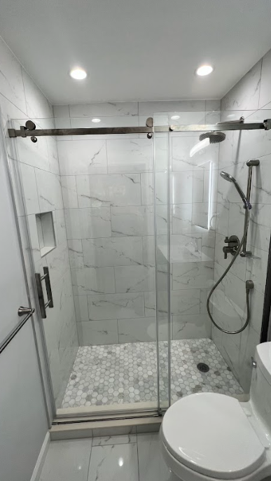 A bathroom with a toilet , shower , and sliding glass door.