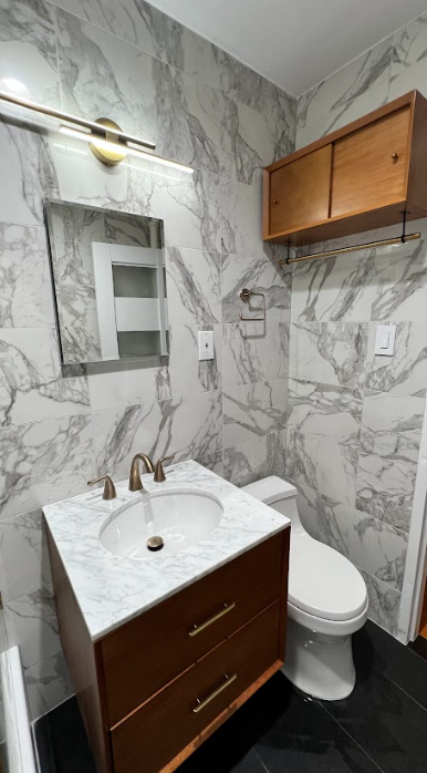 A bathroom with a sink , toilet , mirror and marble walls.