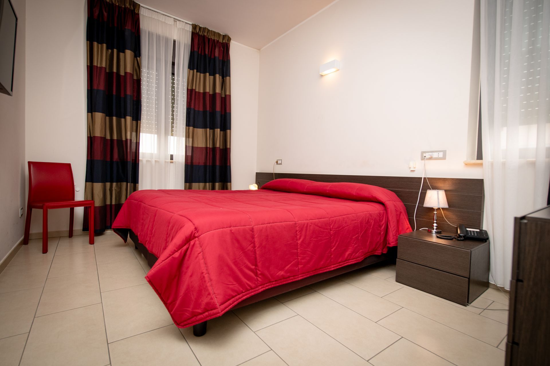 Un letto con una coperta rossa in una stanza d'albergo