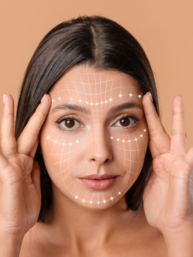 Front-facing woman with a facial grid overlay and hands framing her temples.